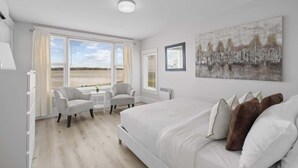 A bedroom with a large bed, two chairs, a small table, and a window with a view.