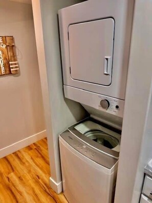 A compact laundry room with a washing machine and dryer stacked vertically. - Waterfront Cozy 1 Bedroom  Condo Downtown Ch'town (Charlottetown)