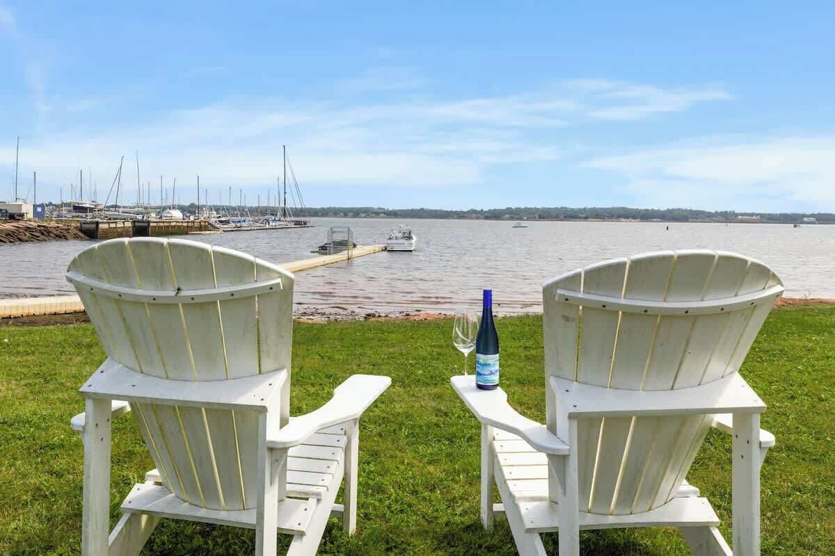 Zwei weiße Adirondack-Stühle mit Blick auf eine Marina, Boote und einen Steg.