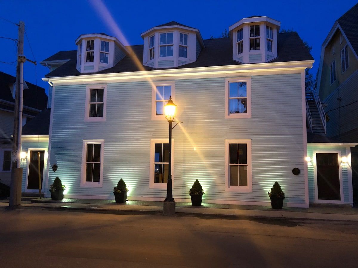 Un bâtiment à deux étages, doté d’un luminaire central, de nombreuses fenêtres et d’une tourelle d’angle.