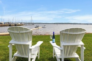 Zwei weiße Adirondack-Stühle mit Blick auf eine Marina, wo Boote liegen, unter einem klaren Himmel.