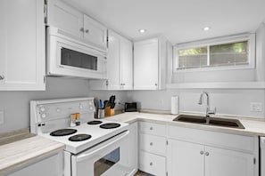 A kitchen with white cabinets, a microwave, a stove with a range hood, a sink, and a window with blinds. - Waterfront Posh King Studio Suite Downtown Ch'town (Charlottetown)