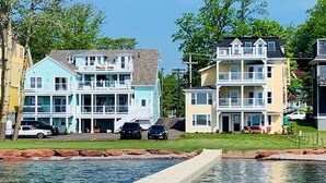 A waterfront property with two multi-story buildings, a swimming pool, and parked cars.