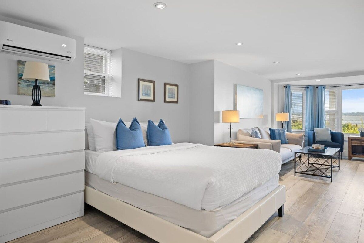 A modern bedroom with a large bed, bedside tables, a sofa, and a view of the outdoors.