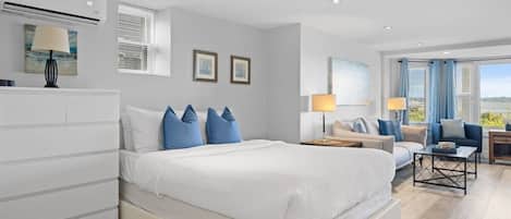 A modern bedroom with a large bed, bedside tables, a sofa, and a view of the outdoors.