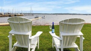Two white Adirondack chairs facing a marina with boats and a dock.