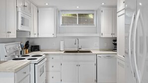 A modern kitchen with white cabinets, a stainless steel refrigerator, a built-in oven, and a window above the sink.