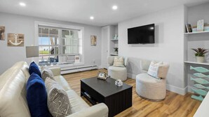 A modern living room with a sofa, armchair, coffee table, and a TV mounted on the wall. - Waterfront Deluxe King Suite Condo Downtown Chtown (Charlottetown)