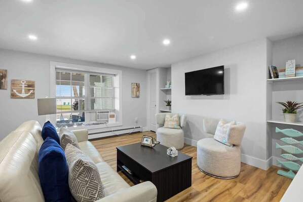 A modern living room with a sofa, armchair, coffee table, and a TV mounted on the wall. - Waterfront Deluxe King Suite Condo Downtown Chtown (Charlottetown)