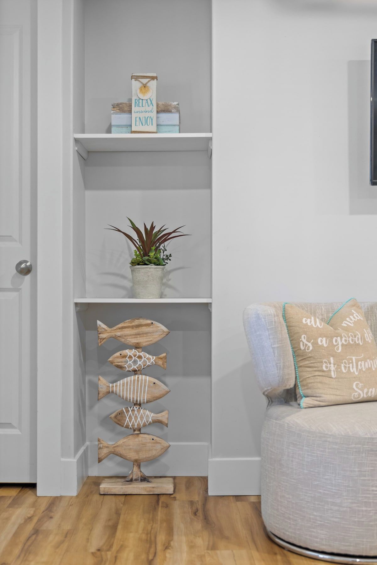 A room with a white door, a shelf with decorative items, a plant, and a couch with a cushion.