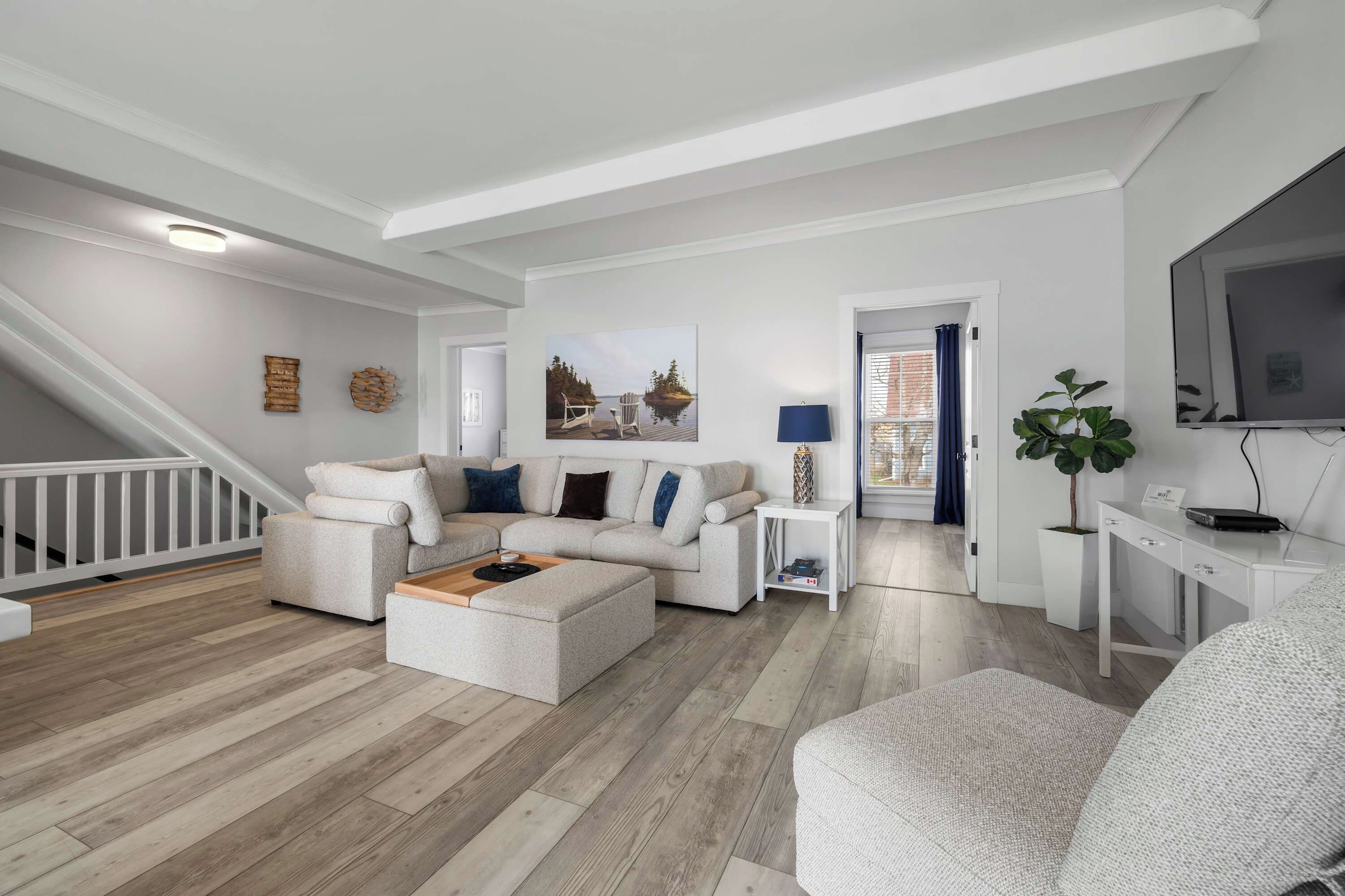 A modern living room with a sofa, ottoman, and a TV. There is a staircase leading to another level.
