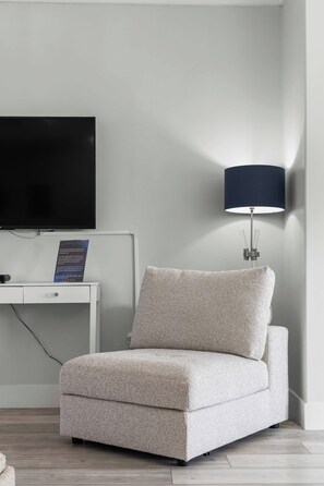 A modern hotel room with a flat-screen TV mounted on a white console, a beige sofa, and a floor lamp. - Beautiful Waterfront 2 Bdrm Condo Downtown Ch'town (Charlottetown)