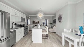 A modern kitchen with stainless steel appliances, a central island, and a dining area with white furniture. - Beautiful Waterfront 2 Bdrm Condo Downtown Ch'town (Charlottetown)