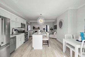 A modern kitchen with stainless steel appliances, a central island, and a dining area with white furniture. - Beautiful Waterfront 2 Bdrm Condo Downtown Ch'town (Charlottetown)