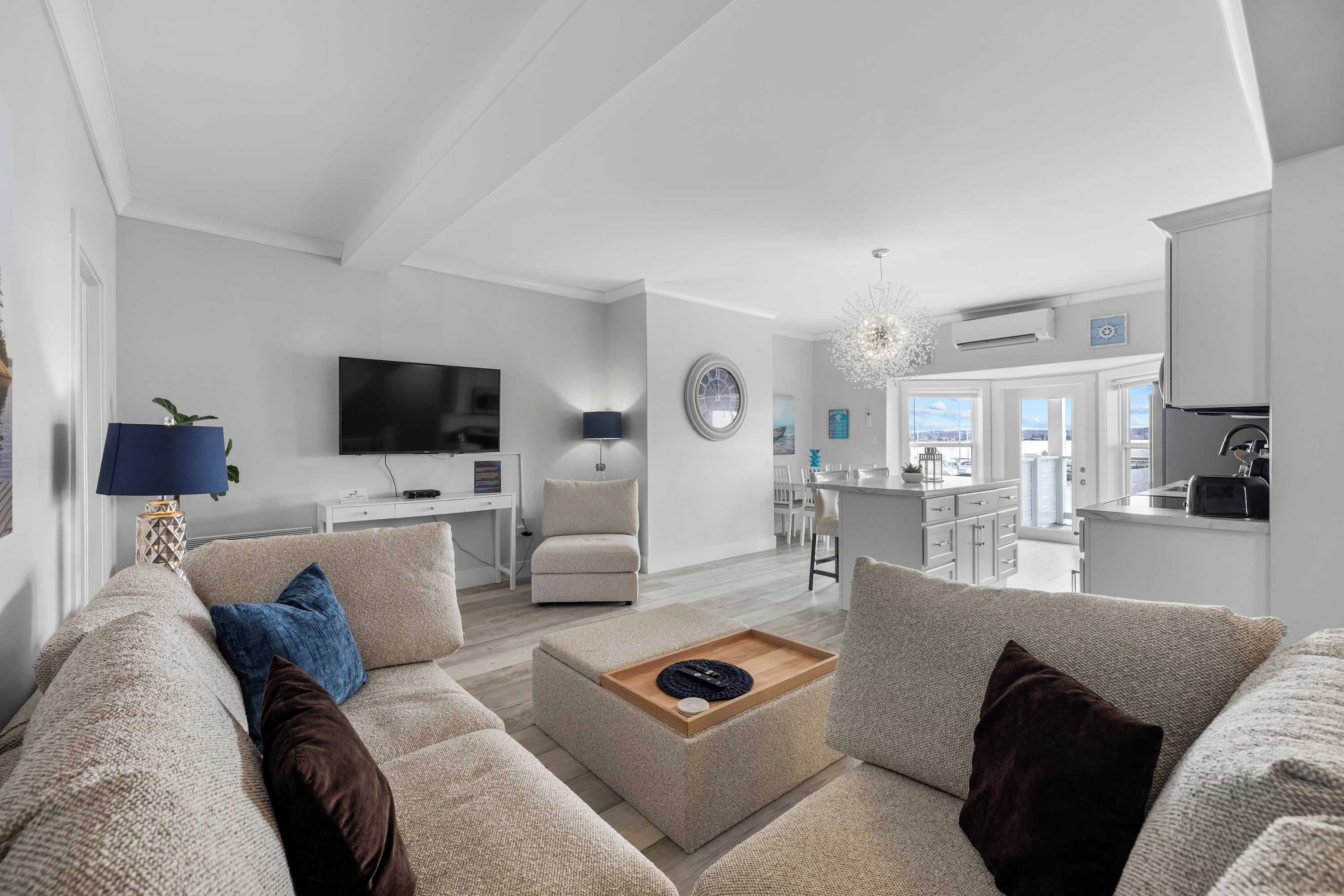 Ein modernes Wohnzimmer mit einer Couch, einem Couchtisch, einem Fernseher und einer Küche im Hintergrund.