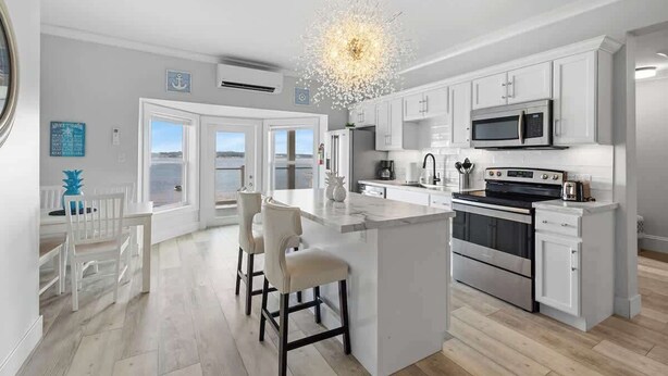A modern kitchen with white cabinetry, a central island with bar stools, a built-in oven, and a microwave. - Beautiful Waterfront 2 Bdrm Condo Downtown Ch'town (Charlottetown)