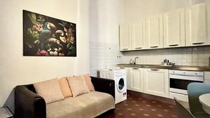 Ein kompakter Wohnraum mit Sofa, Waschmaschine, Esstisch und Küchenzeile inklusive Schränken und Spüle.
