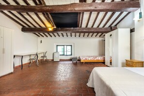Une pièce avec des poutres apparentes, un sol en briques, un lit, un bureau et une fenêtre.