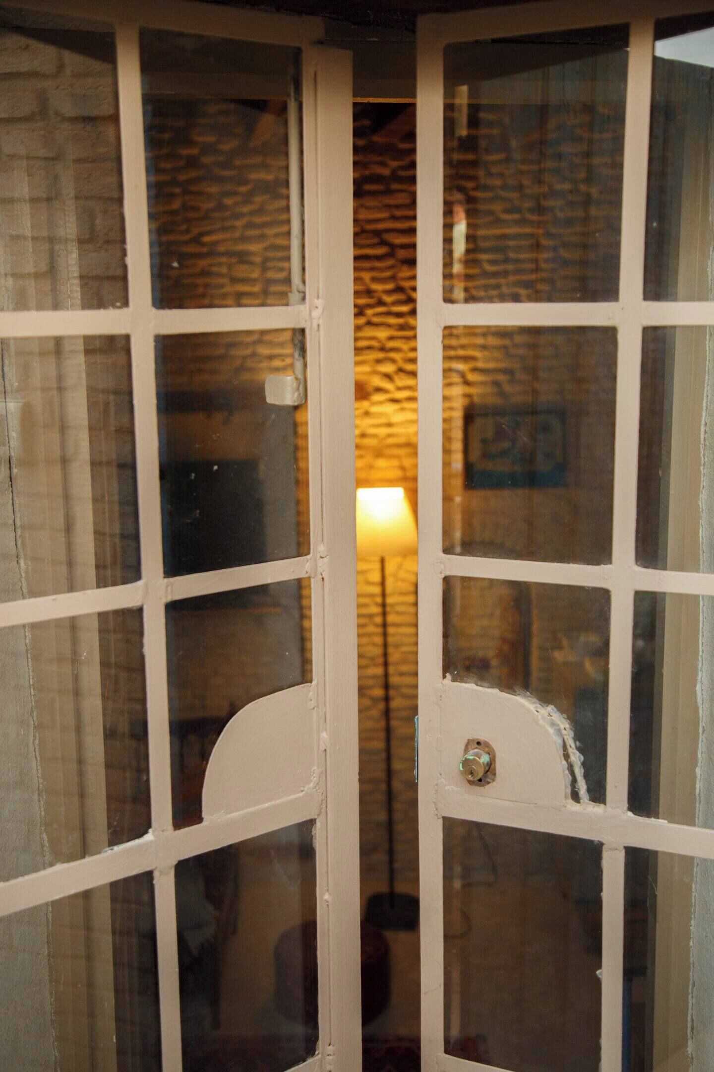 Une fenêtre à cadre blanc, avec un loquet visible et le reflet d’une lampe en arrière-plan.