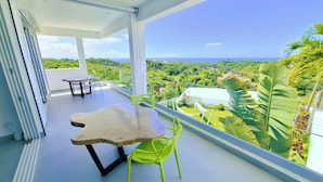 Un balcon agrémenté d’une table et de chaises, offrant une vue sur un paysage luxuriant et l’océan.