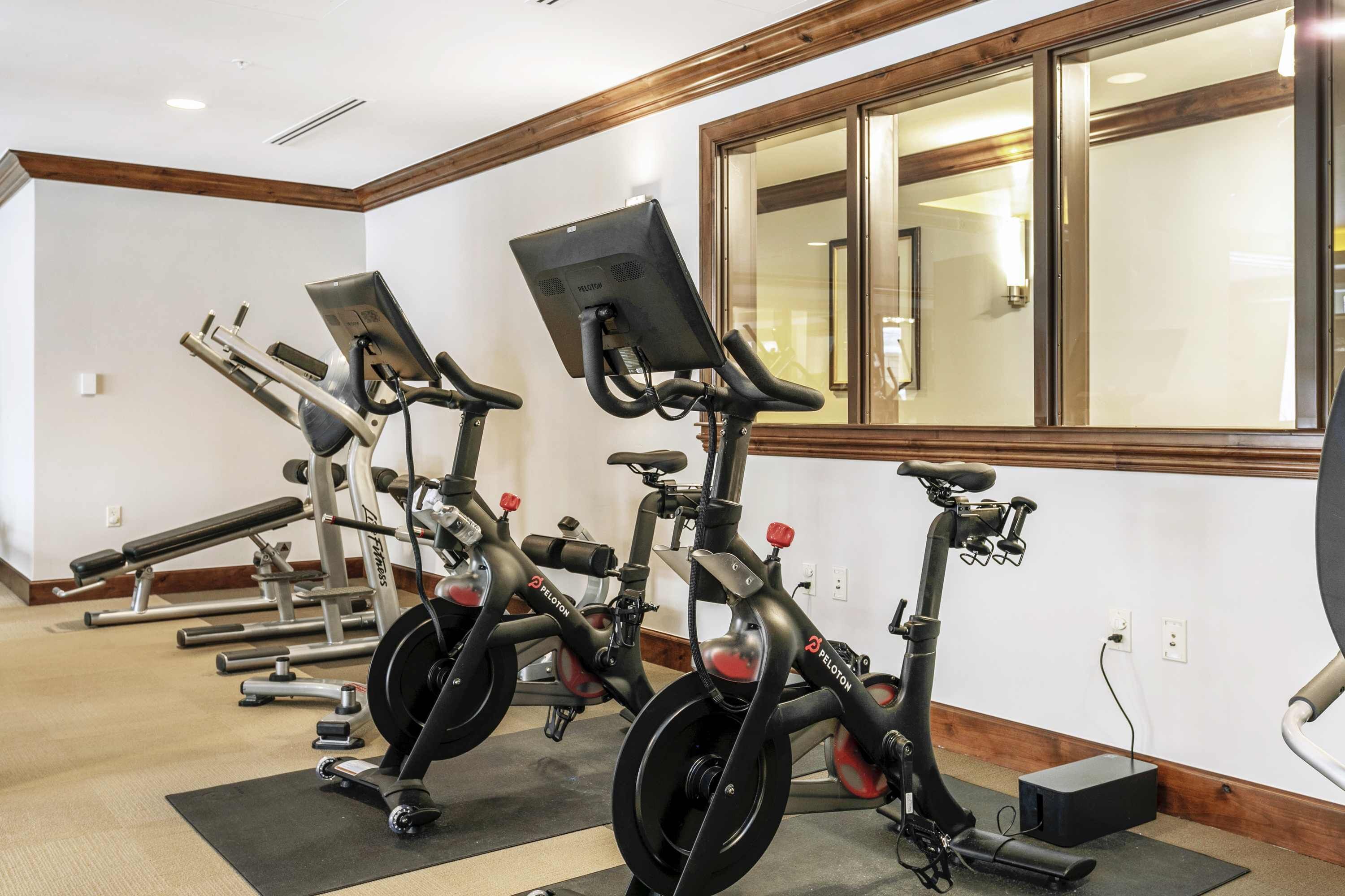 A row of stationary bikes in a gym with wooden trim and a large mirror on the wall.