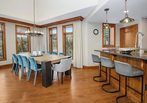A spacious dining area with a wooden table and blue chairs, large windows with curtains, and a kitchen area with bar stools. - Spectacular Ritz Carlton Penthouse Residence in Vail. Two levels!! (Vail)