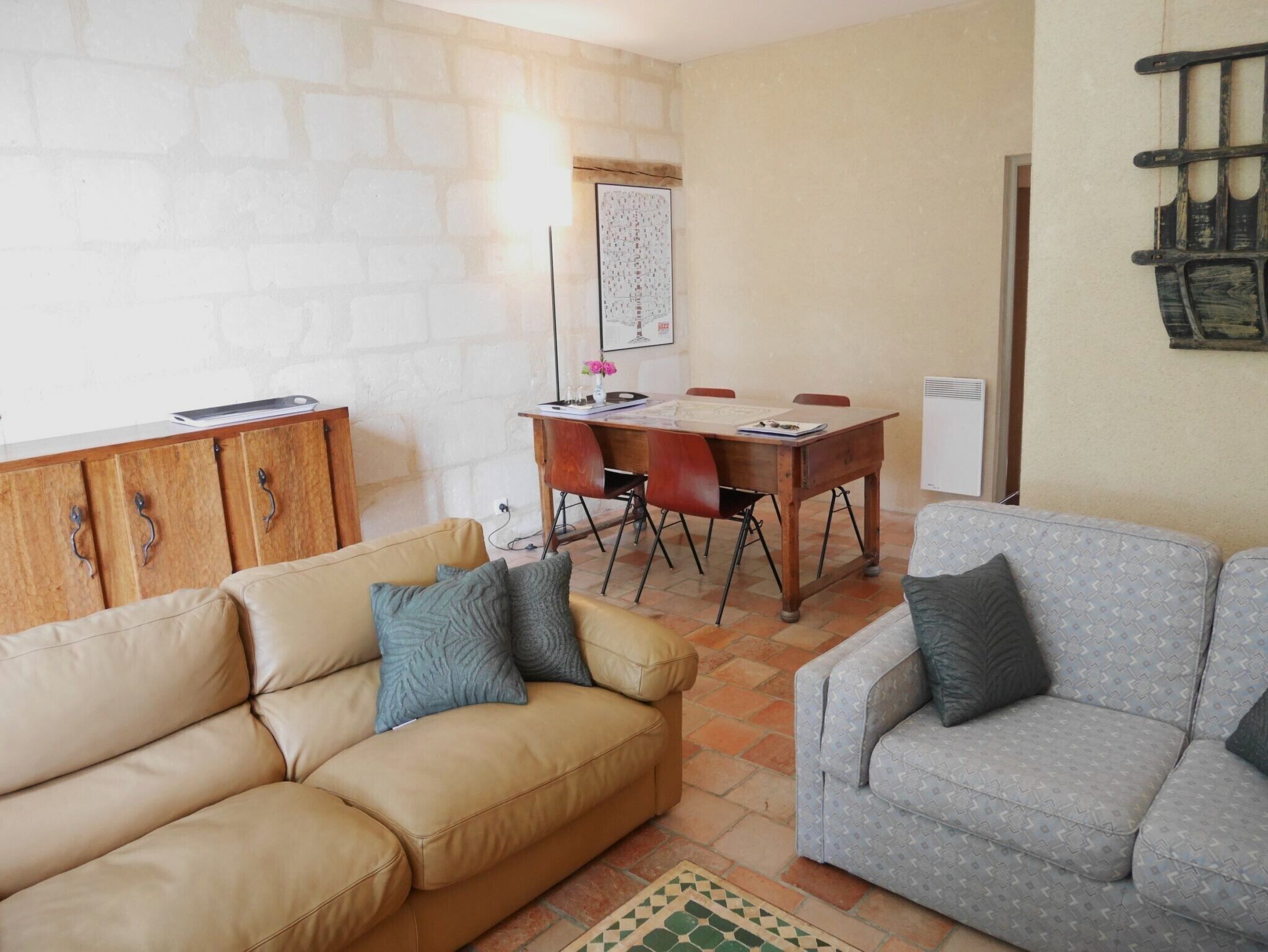 A living room with a beige sofa, a grey patterned sofa, a wooden cabinet, and a dining table with chairs.