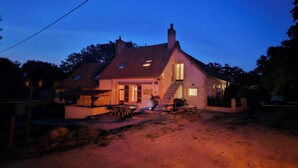 Een huis met een schuin dak, schoorsteen en een voortuin met een tafel en stoelen.