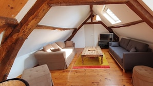 Een zolderkamer met een hoogslaper, een bank, een salontafel en een televisie.