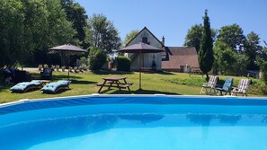 A backyard with a swimming pool, lounge chairs, a picnic table, and a house with a tiled roof.