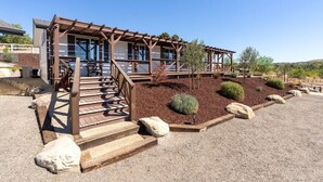 A building with a wooden pergola entrance, a gravel driveway, and landscaped garden beds with shrubs and rocks. - River Road Retreat! Hot Tub +  Barndominium (Templeton)