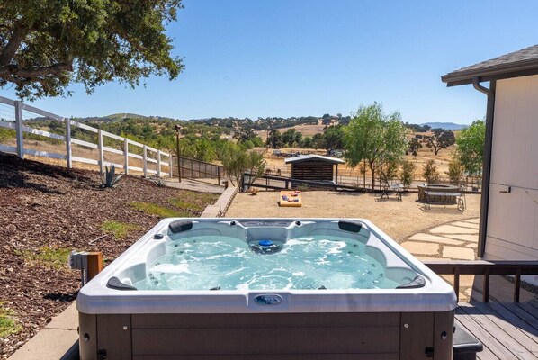 A hot tub in a backyard with a view of a hilly landscape and a fenced area.