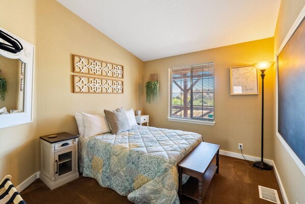 A bedroom with a bed, bedside table, nightstand, and a window with blinds.