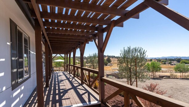 A wooden deck with a pergola, overlooking a dry landscape with sparse vegetation and distant hills. - River Road Retreat! Hot Tub +  Barndominium (Templeton)