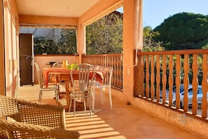 A balcony with a table and chairs, a wicker chair, and a view of a car and trees.