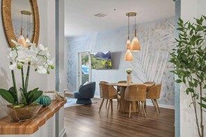 A dining area with a table and chairs, a hanging light fixture, and a plant.