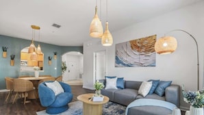 Una sala moderna con un sofá azul, una mesa de centro redonda y lámparas colgantes de mimbre.