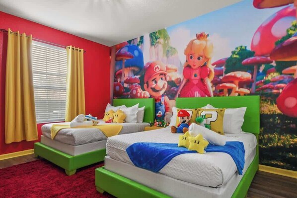 Una habitación con dos camas, paredes rojas, cortinas amarillas y un mural con temática de Mario.