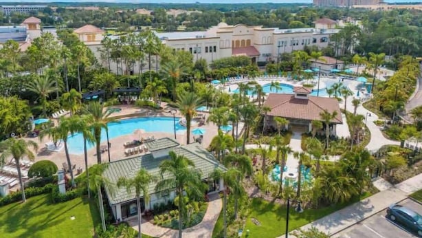 Un resort con varias piscinas, palmeras y un edificio grande al fondo.
