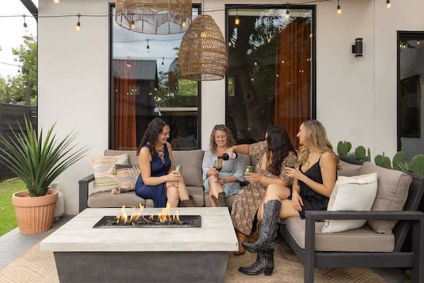 Un grupo de personas sentadas en un sofá y alrededor de un brasero en un patio al aire libre.
