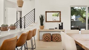 Una cocina moderna con encimera blanca, mesa de comedor de madera y una escalera.