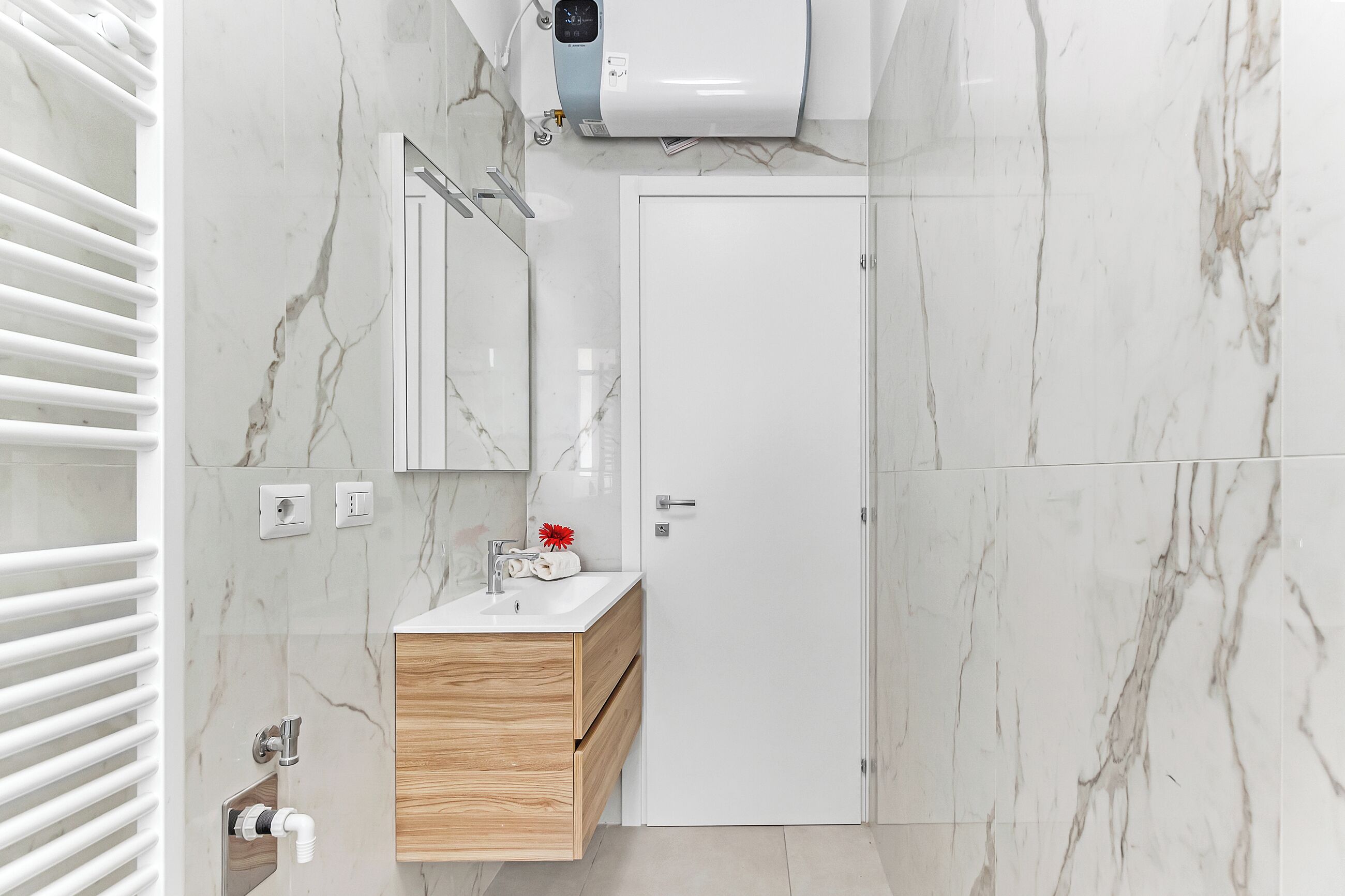 Un bagno moderno con un mobile lavabo bianco, pareti in marmo, un appendi asciugamani, un distributore di asciugamani e un soffione.