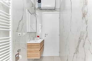 A modern bathroom with a white vanity, marble walls, a towel rack, a towel dispenser, and a showerhead. - Alessia's Flat - Caroli (Milan)
