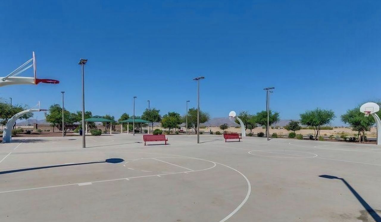An outdoor basketball court with clear markings, benches, and street lamps.