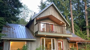 Une maison en bois à deux étages, dotée d’un balcon, de grandes fenêtres et d’un escalier menant à l’entrée.
