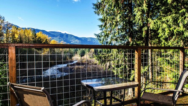 Une table et des chaises en verre sur un balcon offrant une vue sur une montagne et une forêt.