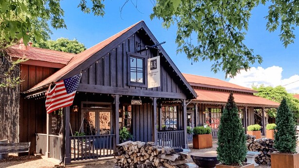 Ein rustikales Holzhaus mit Veranda, einer amerikanischen Flagge und einem Schild mit der Aufschrift 'OPEN'.