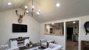 Ein Wohnzimmer mit einem aufgehängten Hirschgeweih, einem Chandelier, einem Fernseher und einem karierten Teppich.