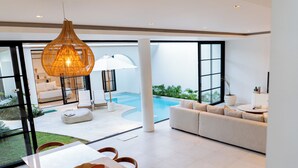 A modern interior with a pool, a sofa, and a dining area. - Villa Janoor by GORO (Keroboken Kelod)
