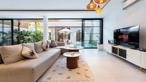 A modern living room with a sofa, coffee table, TV, and large windows. - Villa Janoor by GORO (Keroboken Kelod)